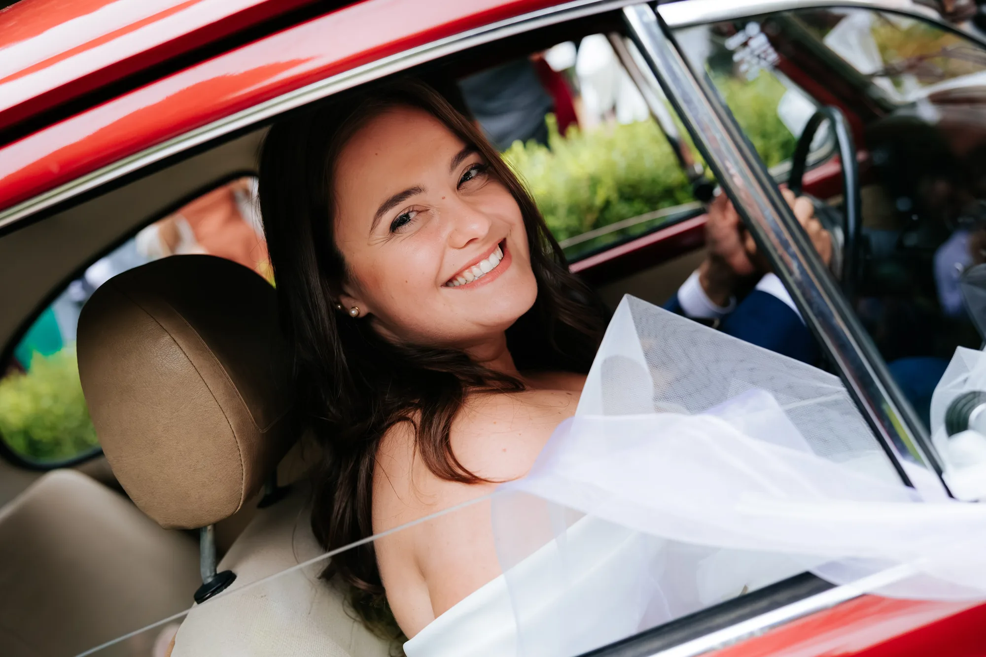 Il sorriso della sposa affacciata a un’auto rossa — Luméa Wedding